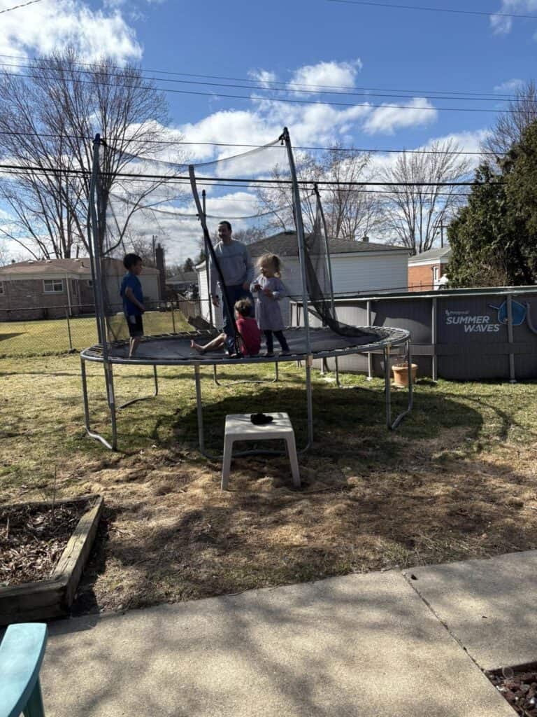 A personal post of a sunny day captures three children and an adult on a backyard trampoline, while a black-and-white cat lounges on a nearby table under the partly cloudy sky.