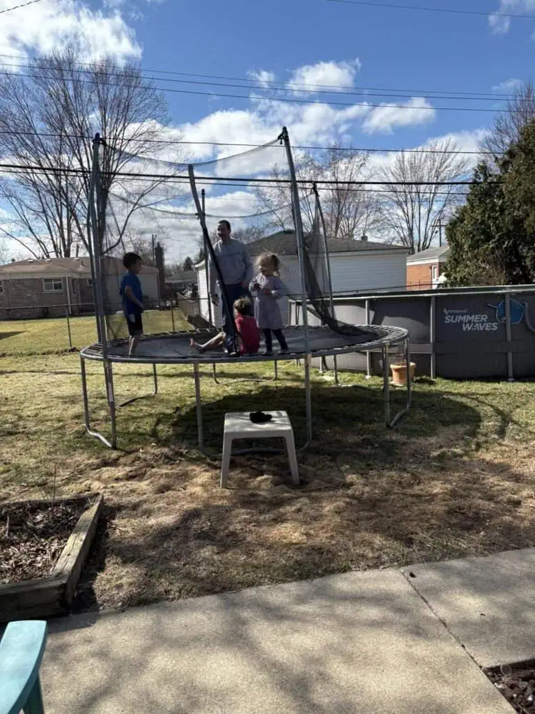 A personal post of a sunny day captures three children and an adult on a backyard trampoline, while a black-and-white cat lounges on a nearby table under the partly cloudy sky.