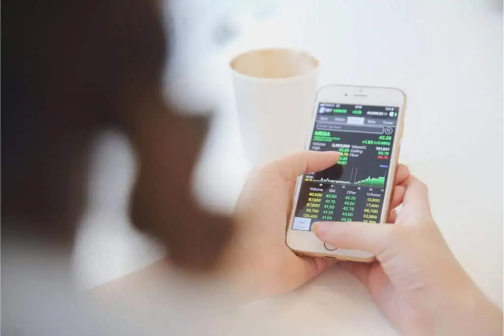 A person using a smartphone to check stock market data, carefully analyzing figures for their retirement planning, with a cup beside them.