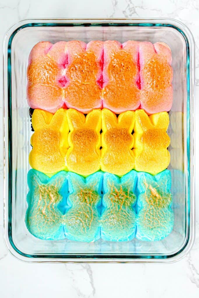 Colorful Peeps marshmallow bunnies in rows of pink, yellow, and blue sit snugly in a glass baking dish on a white surface, ready for your next Easter Bunny-inspired s'mores dip creation.