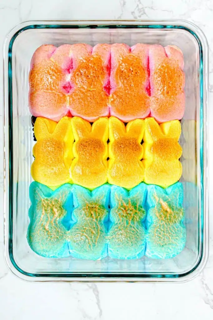 Colorful Peeps marshmallow bunnies in rows of pink, yellow, and blue sit snugly in a glass baking dish on a white surface, ready for your next Easter Bunny-inspired s'mores dip creation.