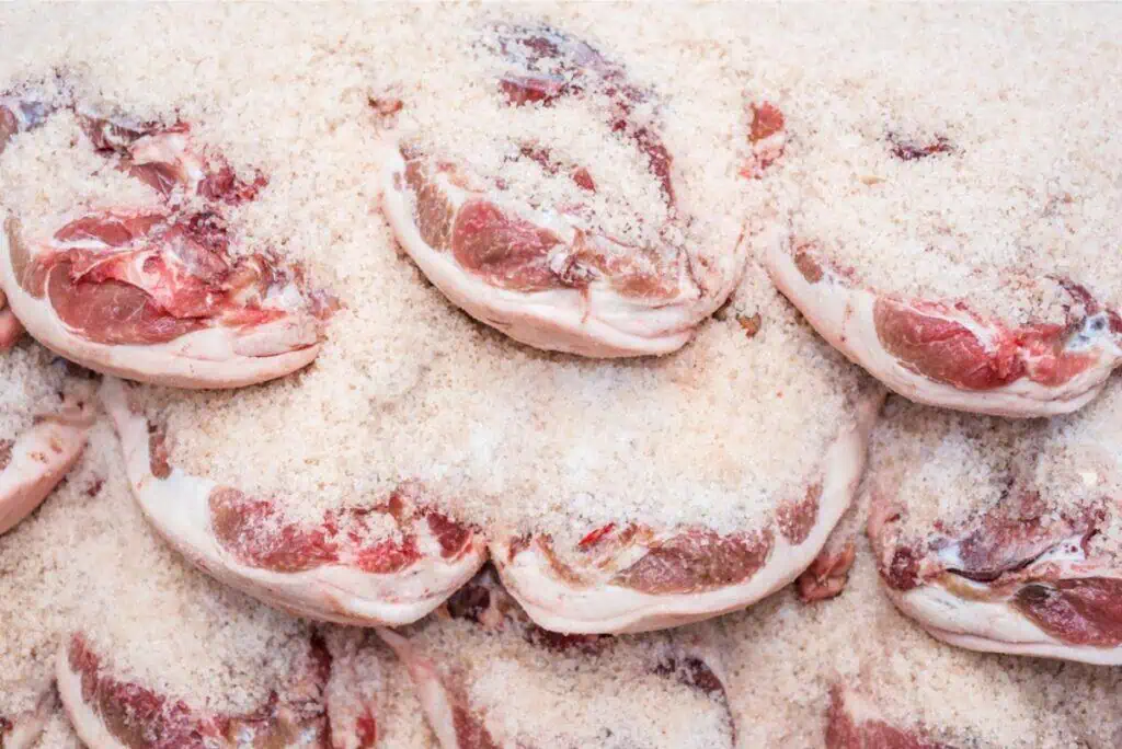 Slices of raw meat, carefully salted for preservation without a refrigerator, are neatly arranged in a stack.