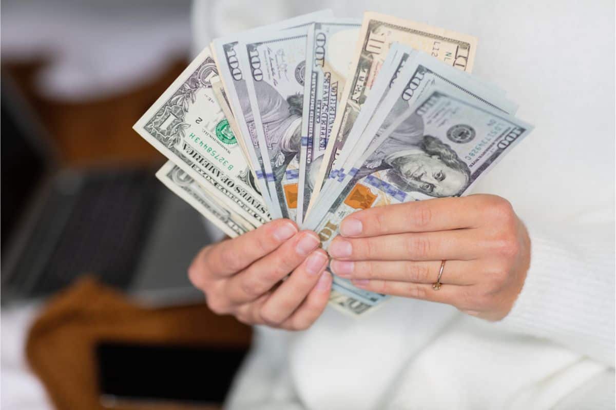 A person showcases a fan of U.S. dollar bills in various denominations, grasping the essence of how to save money in today's Internet-driven world.