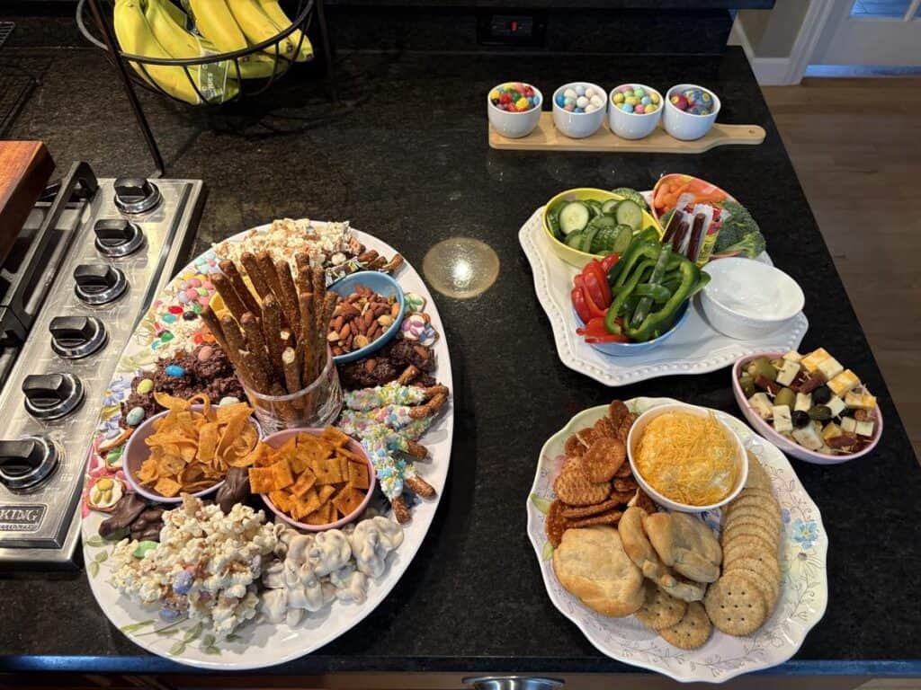 A personal post featuring a kitchen counter lined with assorted snack platters—pretzels, popcorn, chips, crackers, cheese, veggies, candies—and a tray of bananas in the background.