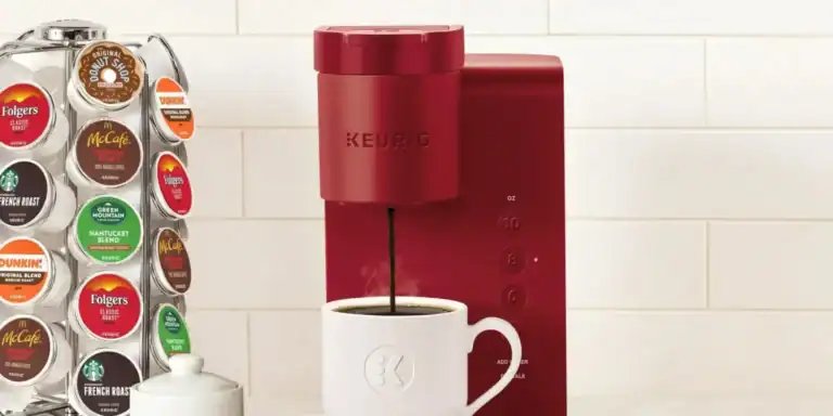 A vibrant red Keurig coffee maker dispenses rich coffee into a white mug, accompanied by a spoon. A coffee pod holder filled with assorted pods sits to the left against a pristine white tile backsplash, offering endless choices for your perfect brew.