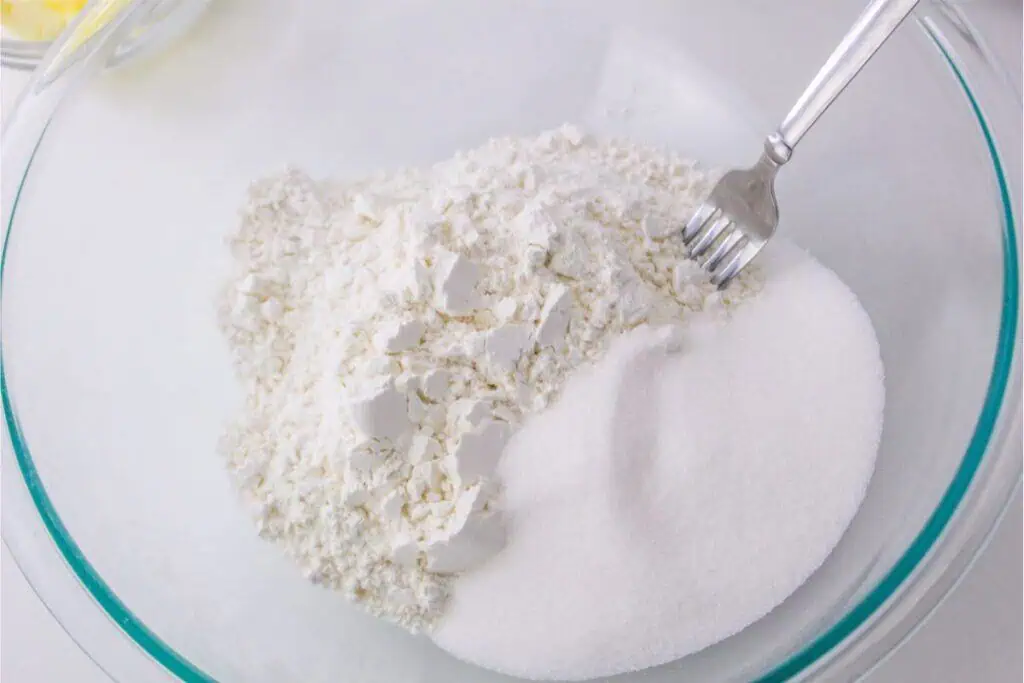 A glass bowl containing a pile of flour and sugar, perfect for a scone recipe, with a fork resting on top.