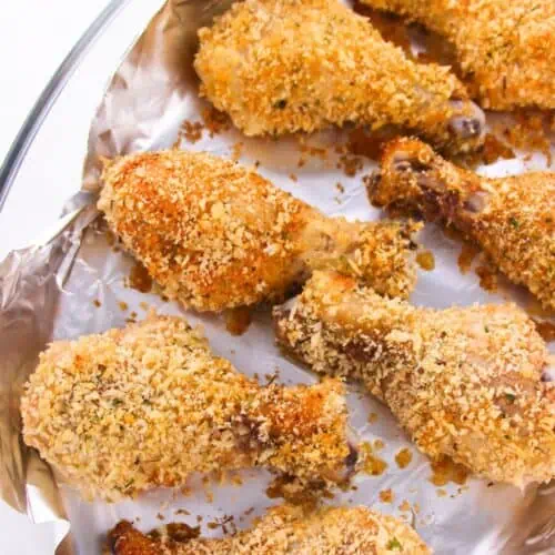 Baked breaded chicken drumsticks on a foil-lined baking dish boast a golden-brown, crispy coating inspired by homemade shake and bake.
