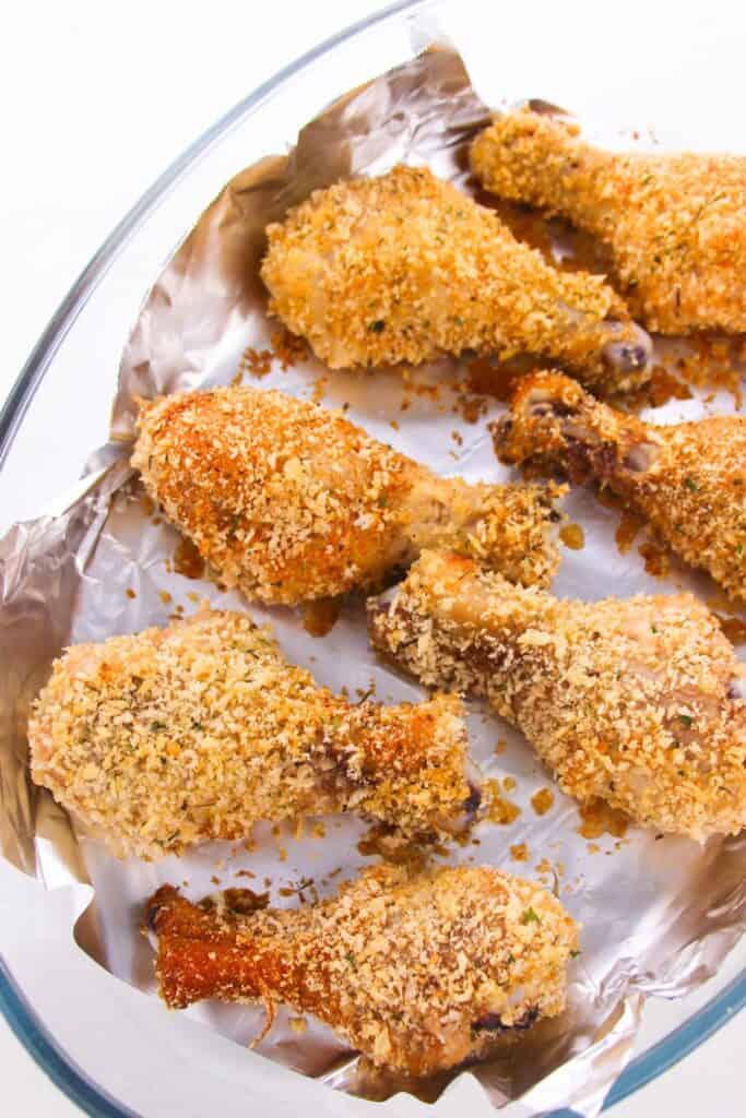 Baked breaded chicken drumsticks on a foil-lined baking dish boast a golden-brown, crispy coating inspired by homemade shake and bake.