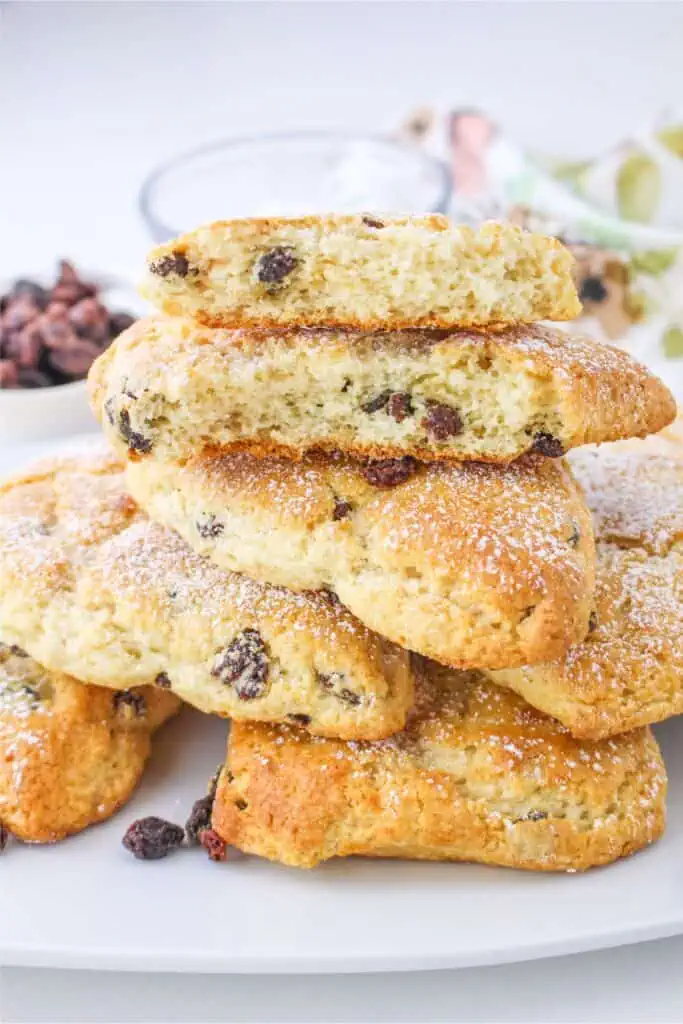 A stack of easy and delicious scones with raisins, dusted with powdered sugar, placed on a white plate. One scone is broken, showing a light, fluffy interior that makes this Bisquick recipe simply irresistible.