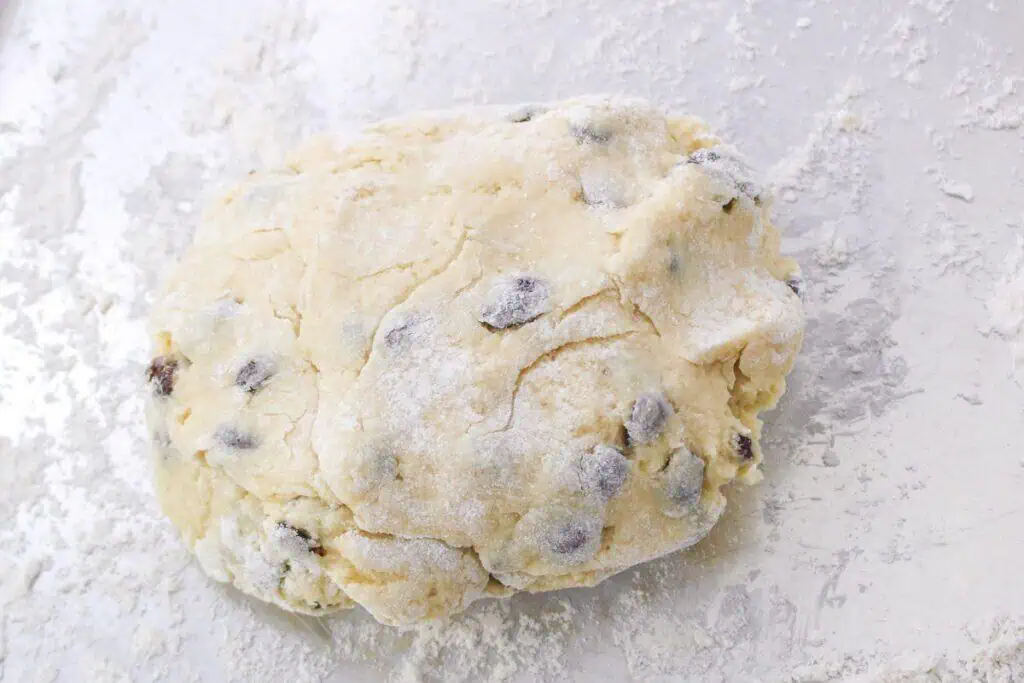 A mound of raw cookie dough with chocolate chips, reminiscent of a delightful scone, is placed on a lightly floured surface.