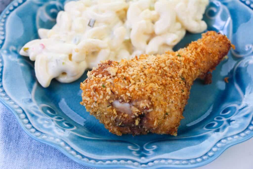 A crispy, homemade shake and bake chicken drumstick sits alongside creamy macaroni salad on a blue plate.