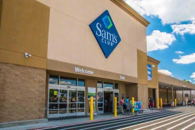 The exterior of a Sam's Club store with customers entering and exiting through the glass doors under a blue sign on a sunny day, where shoppers take advantage of exclusive Sam's Club Membership Deals.