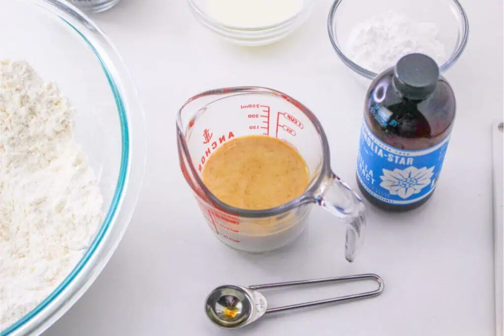 Mixing ingredients on a countertop: flour in a bowl, Bisquick in a measuring cup, vanilla extract bottle, and measuring spoons. An easy scone recipe ready to create delicious treats with minimal fuss.