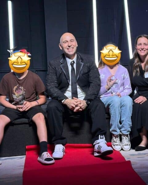 Personal Post: Four people sit on a platform against a dark background with vertical lights; two children's faces are covered with smiley face emojis.