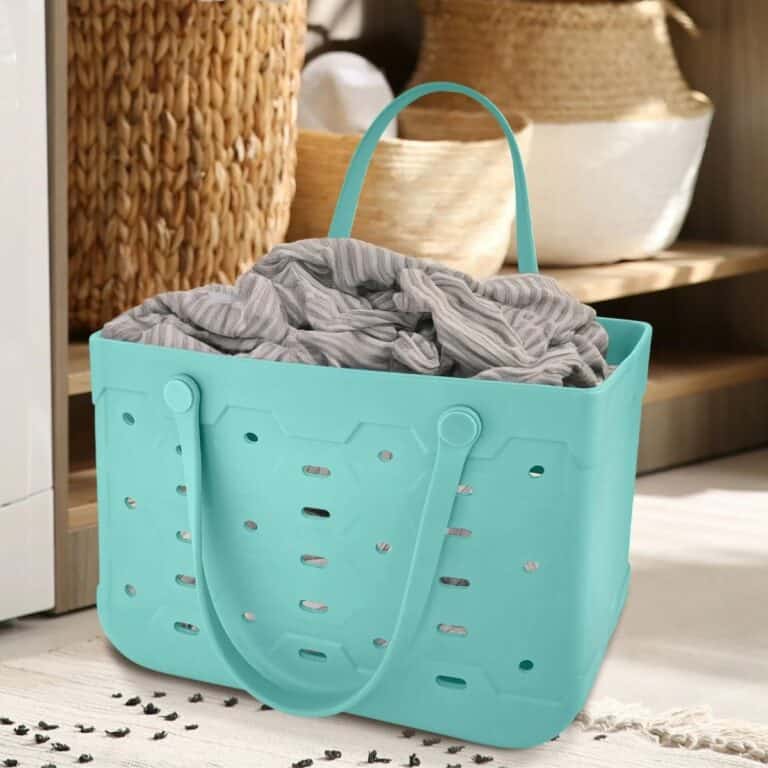A teal plastic laundry basket with holes and handles, reminiscent of a Free Bogg Bag Dupe, holds a gray and white striped fabric, placed on a rug in a room with woven baskets in the background.
