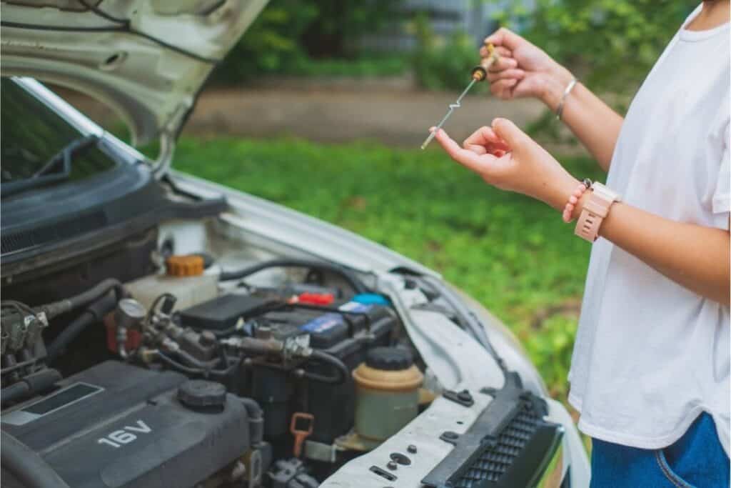 Person checking a car engine’s oil level with a dipstick beneath an open hood—an essential life skill and practical example of everyday life skills.