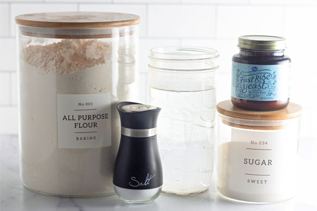 a jar of flour, a jar of water, a salt shaker, a jar of sugar, and a jar of fast rise yeast.