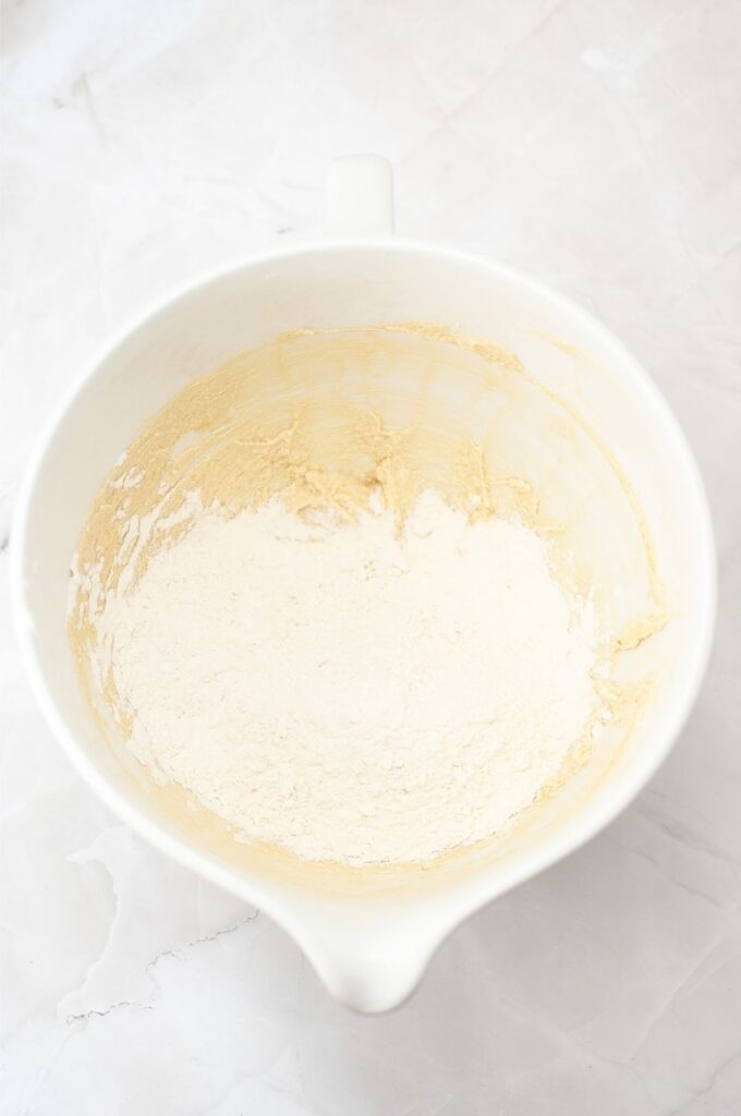 A white mixing bowl containing partially mixed flour and batter on a light marble surface—perfect for starting your favorite homemade cookies or classic vanilla wafers recipe.