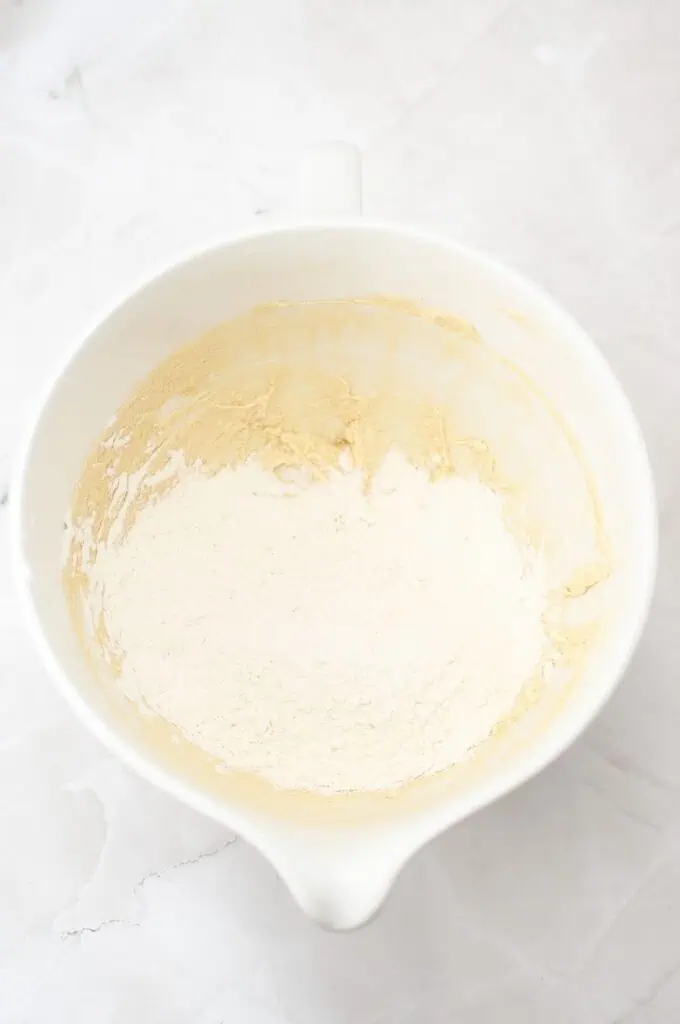 A white mixing bowl containing partially mixed flour and batter on a light marble surface—perfect for starting your favorite homemade cookies or classic vanilla wafers recipe.