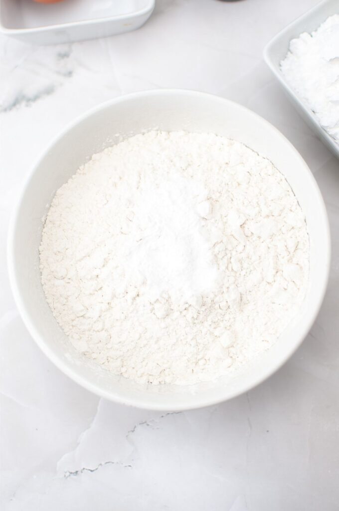 A white bowl filled with flour and a small mound of baking powder, ready for your Homemade Vanilla Wafers, sits on a white marble surface.