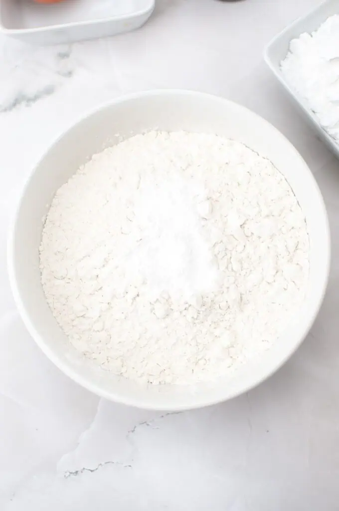 A white bowl filled with flour and a small mound of baking powder, ready for your Homemade Vanilla Wafers, sits on a white marble surface.