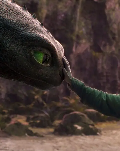 A young person gently touches the nose of a large dragon in a forest setting, with soft light illuminating both figures, evoking the magic of How to Train Your Dragon.