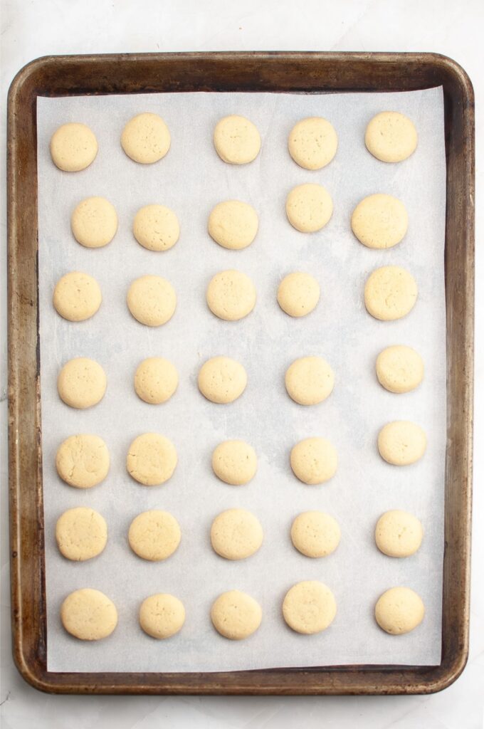 A baking sheet lined with parchment paper holds 35 evenly spaced, unbaked round cookie dough balls—perfect for any homemade cookies recipe.