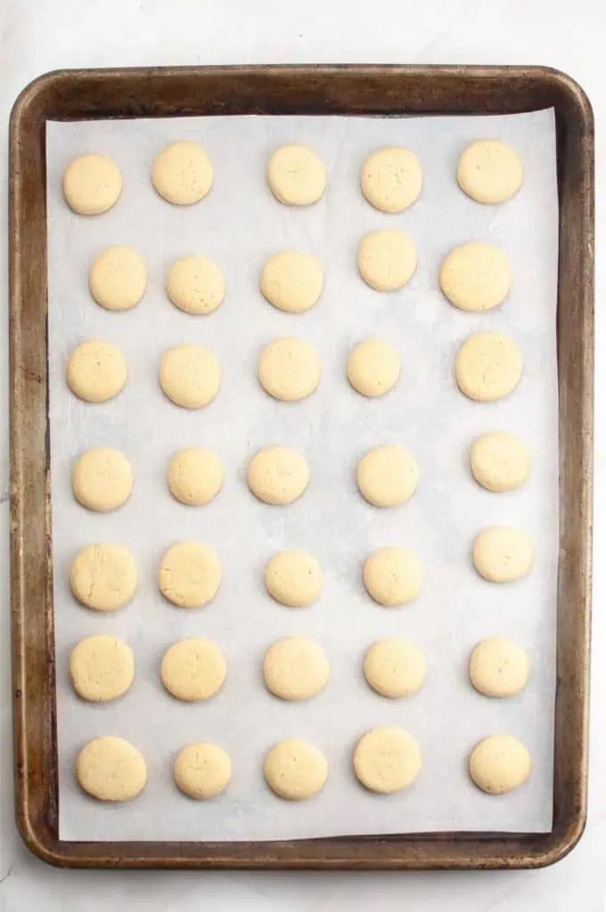 A baking sheet lined with parchment paper holds 35 evenly spaced, unbaked round cookie dough balls—perfect for any homemade cookies recipe.