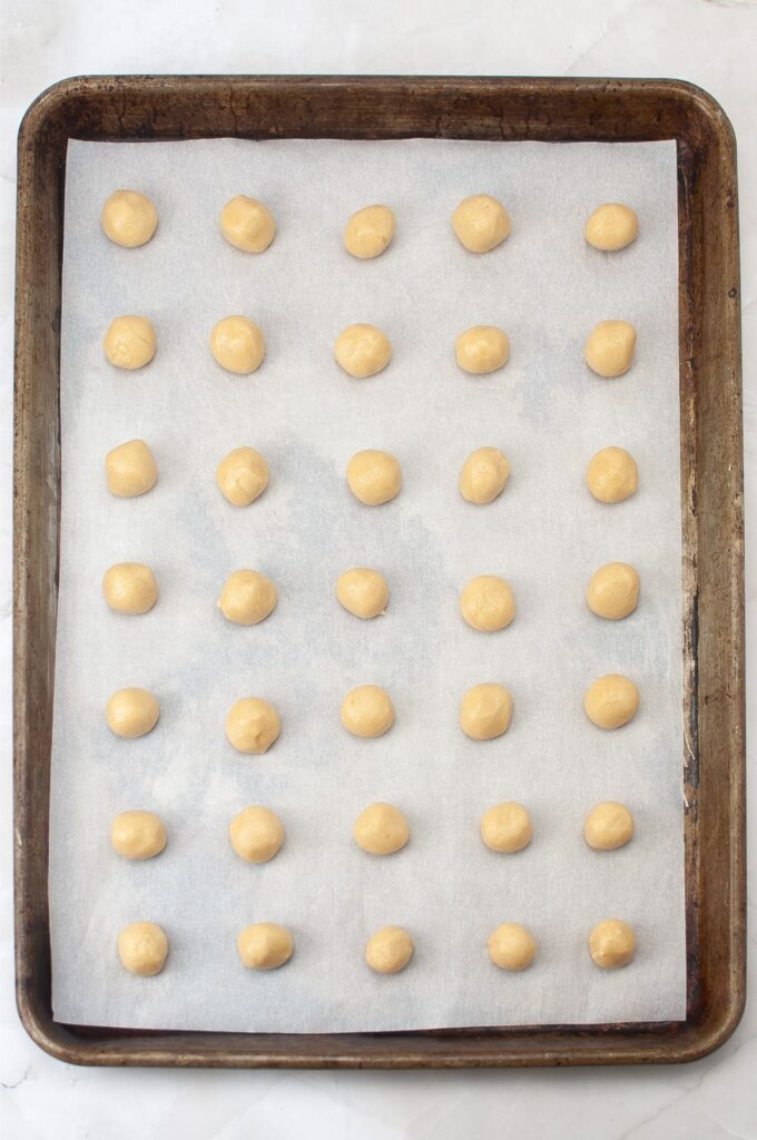 A baking sheet lined with parchment paper holds evenly spaced rows of small, round balls of raw dough, ready to become delicious homemade vanilla wafers. Perfect for anyone looking to try a new cookies recipe.