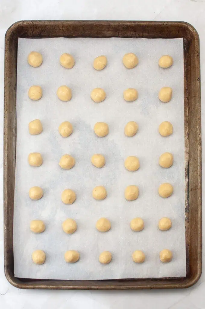 A baking sheet lined with parchment paper holds evenly spaced rows of small, round balls of raw dough, ready to become delicious homemade vanilla wafers. Perfect for anyone looking to try a new cookies recipe.