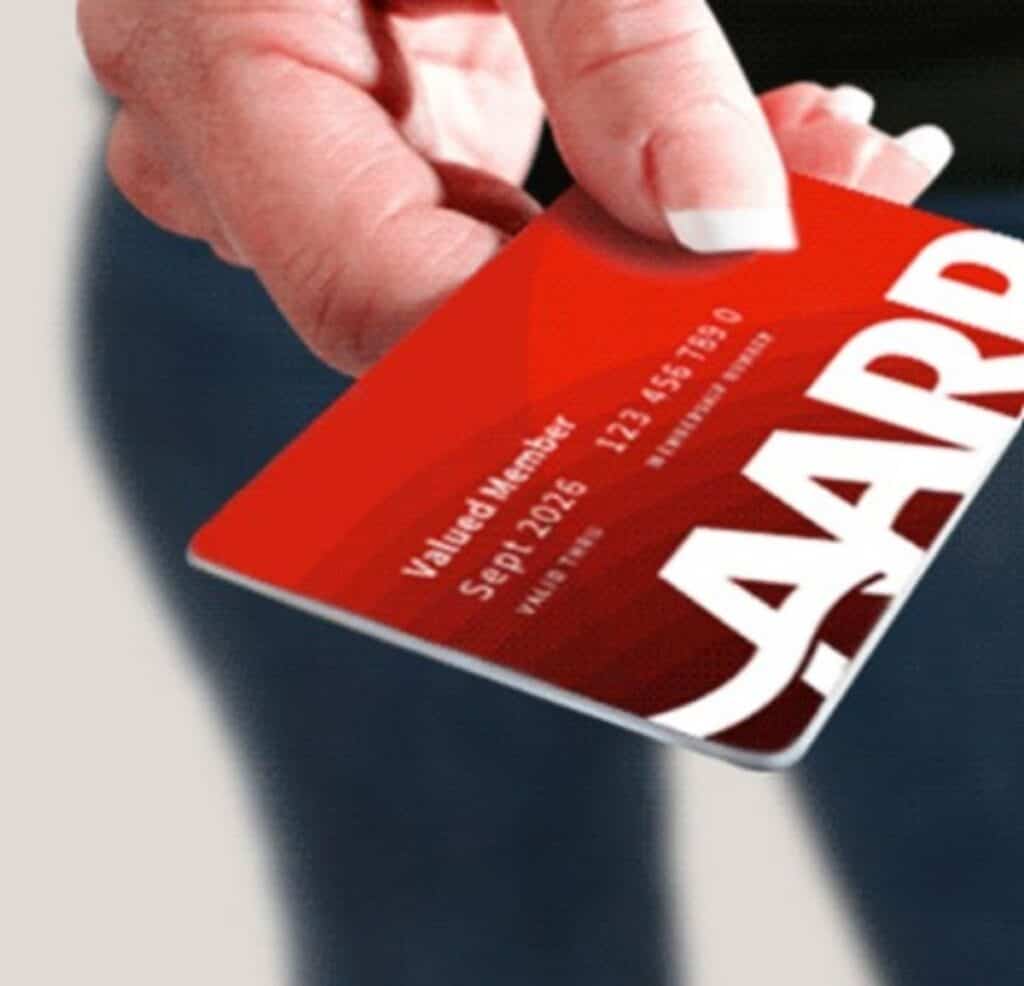 A hand holds a red AARP membership card with white text displaying member information, highlighting an exclusive AARP Membership Deal for Big Savings.
