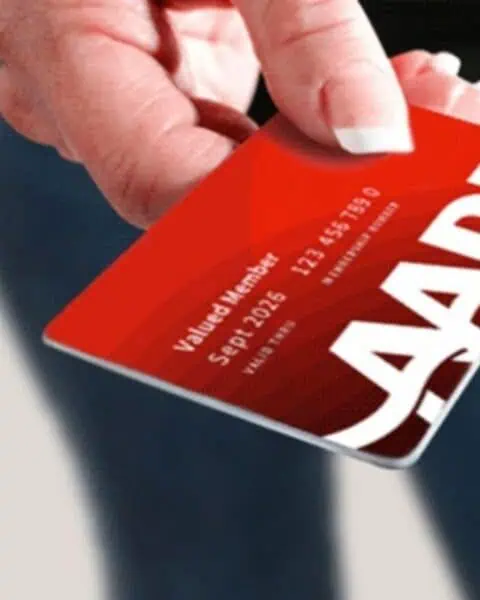 A hand holds a red AARP membership card with white text displaying member information, highlighting an exclusive AARP Membership Deal for Big Savings.