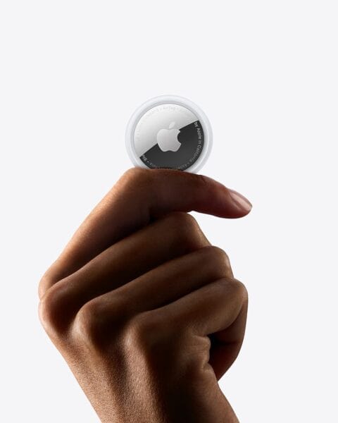 A hand is holding an Apple AirTag between the thumb and index finger against a plain white background, showcasing one of the many ways to use Apple AirTags for tracking your valuables.