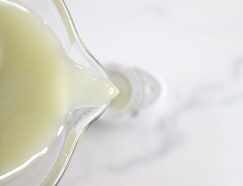 A close-up of milk being poured from a glass jug into a bottle on a white surface, perfect for preparing homemade deodorant or other DIY deodorant recipes.