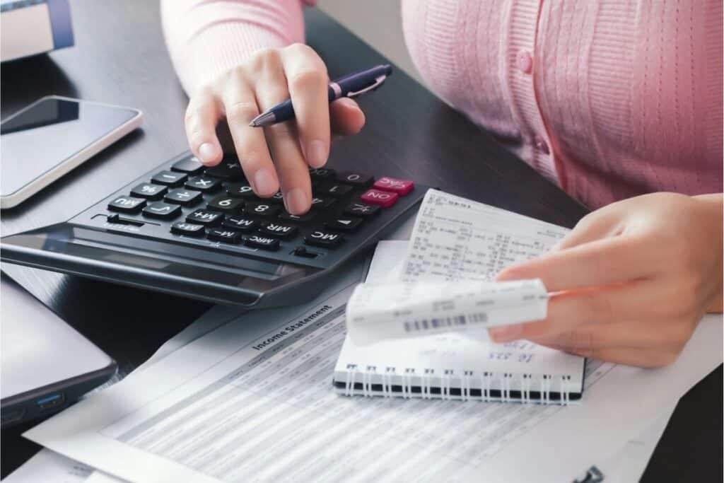 Person using a calculator while holding receipts, with financial documents, a notepad, pen, and smartphone on the desk—focused on debt management and organizing effective loan strategies.