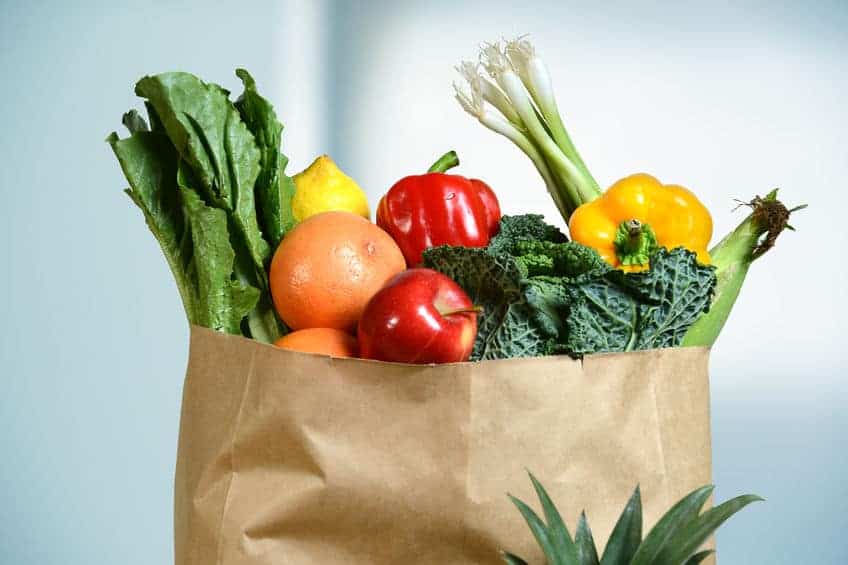 A paper bag filled with fresh produce—including lettuce, citrus fruits, apples, kale, bell peppers, green onions, and a pineapple—offers inspiration for healthy family hacks in the kitchen.