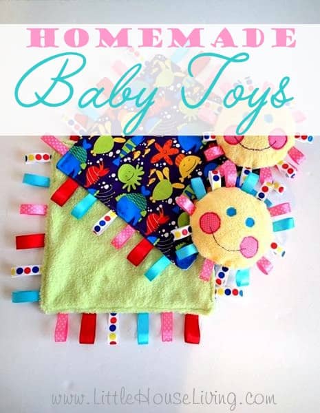 Two colorful homemade baby toys—including a square tag blanket with ribbon loops and two round, smiling sun-shaped plushies—are displayed on a white surface, showcasing creative family hacks for fun and engaging playtime.