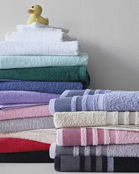 Two stacks of neatly folded towels in various colors are arranged against a light wall, with a rubber duck placed on top of the left stack—a charming touch for any space during the Home Expressions sale.
