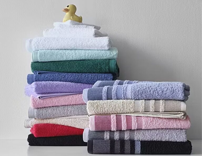 Two stacks of neatly folded towels in various colors are arranged against a light wall, with a rubber duck placed on top of the left stack—a charming touch for any space during the Home Expressions sale.