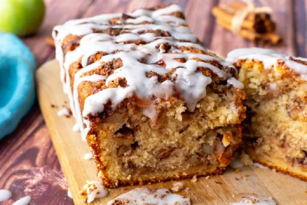 A sliced loaf of cinnamon walnut bread with white icing drizzled on top, resting on a wooden board—perfect for creative apple uses or as inspiration for delicious apple recipes.