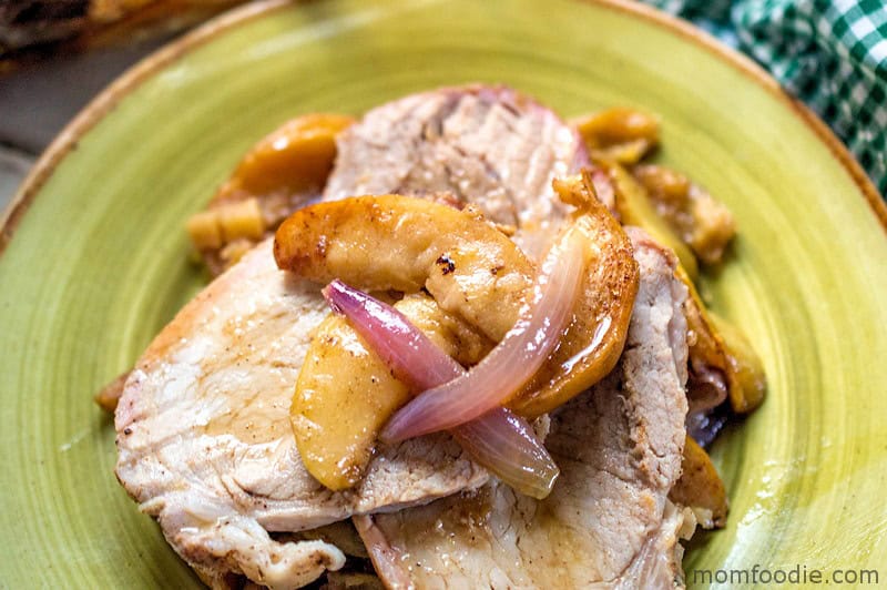 Slices of cooked pork are served with caramelized apple wedges and red onion on a green plate, showcasing one of many creative apple uses for delicious apple recipes.