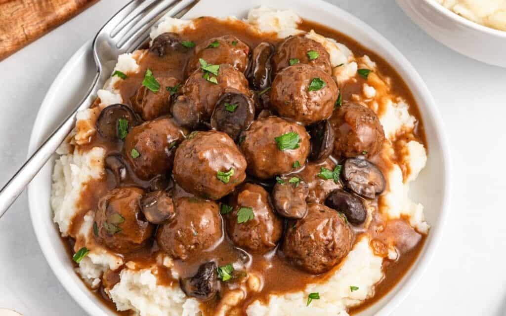 A plate of mashed potatoes topped with meatballs, brown gravy, sliced mushrooms, and chopped parsley—one of those classic Easy Dinner Recipes perfect for cozy nights.