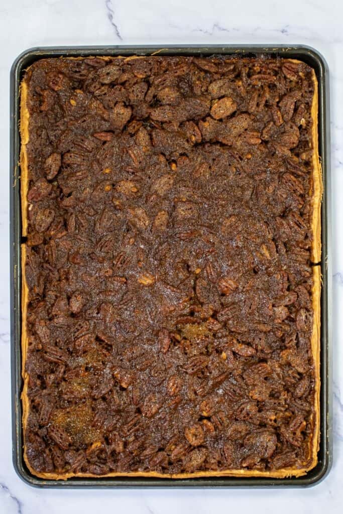 Easy pecan pie dessert bars baked in a large rectangular tray with a visible nut topping, displayed on a marble surface.