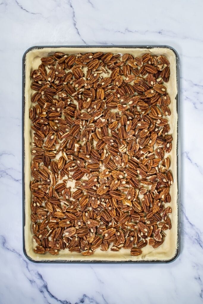 A baking sheet filled with an unbaked pecan dessert bars features a layer of pie crust topped with whole pecans, set on a marble countertop—an easy recipe perfect for Pecan Pie lovers.