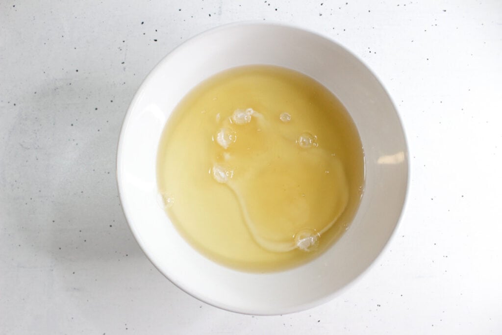 A white bowl containing raw egg whites and yolks on a white surface—perfect for mixing ingredients for an effective DIY grout cleaner.