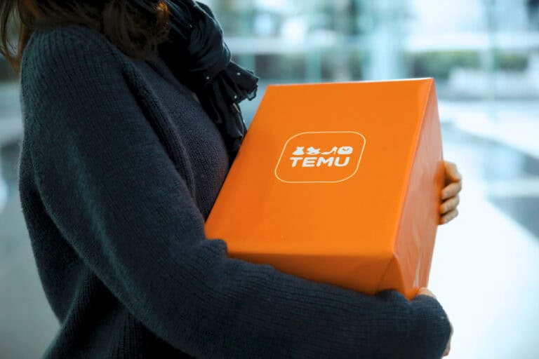 A person in dark clothing holds an orange Temu box indoors, showcasing their latest Temu delivery.