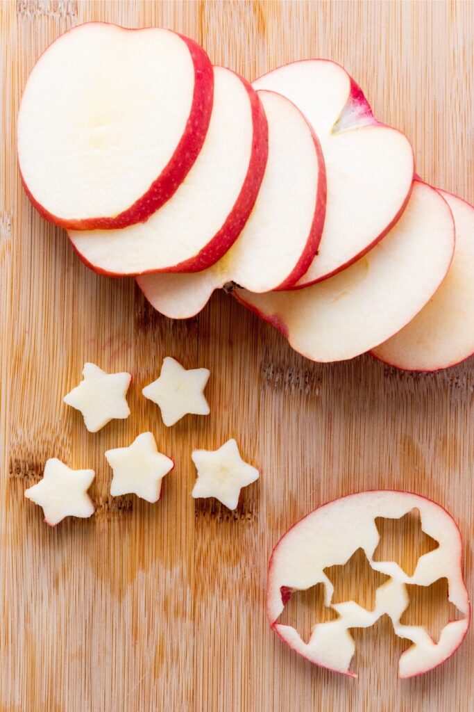 Sliced red apple on a wooden board, with several star-shaped pieces cut out and arranged nearby—perfect for adding to a festive Red White Blue Fruit Salad.