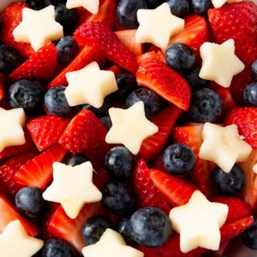 A Red White Blue fruit salad featuring a bowl of sliced strawberries, whole blueberries, and star-shaped pieces of melon.