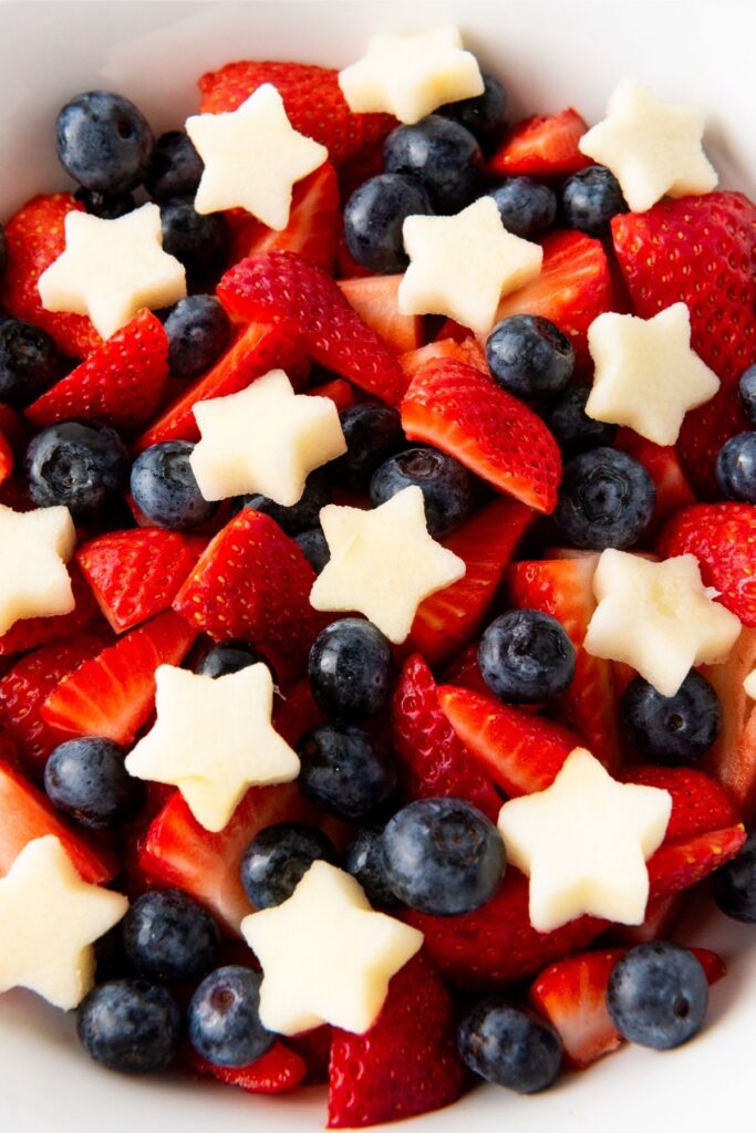 A Red White Blue fruit salad featuring a bowl of sliced strawberries, whole blueberries, and star-shaped pieces of melon.