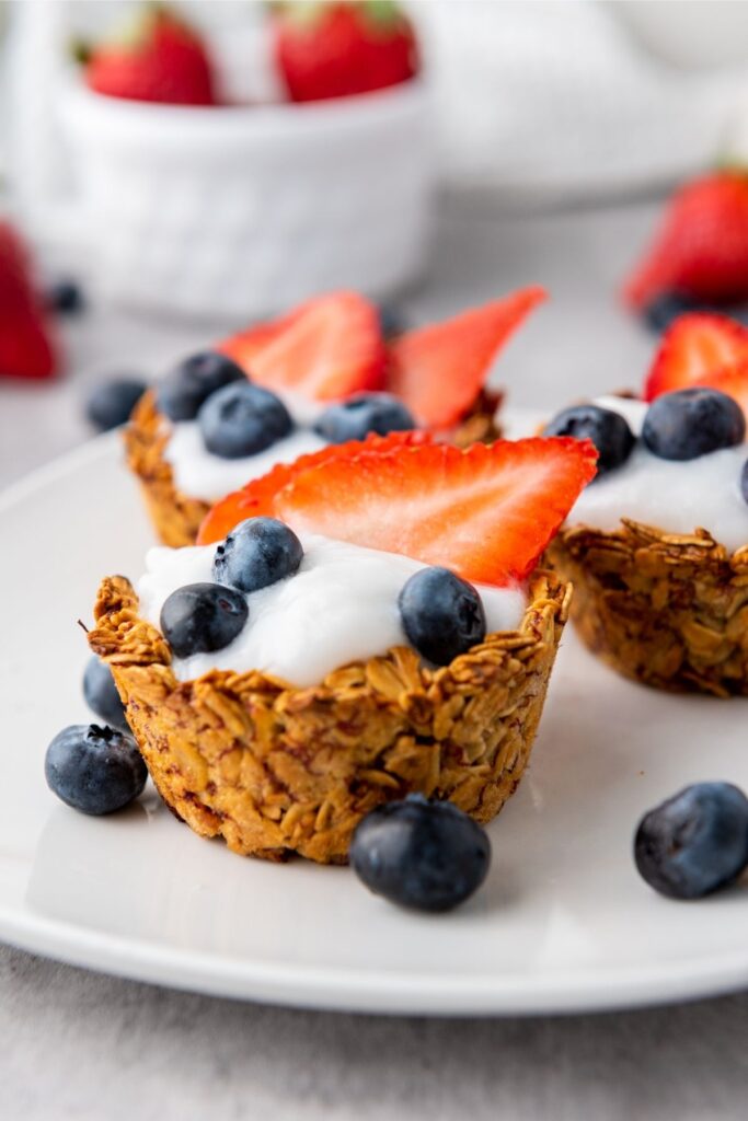 Oatmeal Granola Cups topped with yogurt, sliced strawberries, and blueberries are arranged on a white plate for a delightful Mixed Berry Granola treat.